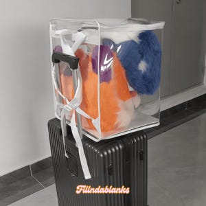 May include: A clear plastic storage bag with a white zipper and a white drawstring. The bag is filled with a blue and orange plush toy. The bag is sitting on top of a black suitcase with a handle.