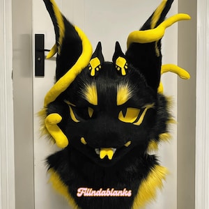 May include: A black and yellow furry creature mask with large ears and yellow accents. The mask has a detailed design with yellow eyes, a mouth, and horns. The text "Fillndablanks" is at the bottom.
