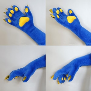 Pu&ograve; includere: Immagine a quattro pannelli di zampe blu pelose con cuscinetti gialli e artigli dorati. Le zampe sono in posizioni diverse, mostrando i dettagli del design. La pelliccia &egrave; di un blu vibrante e gli artigli sono di colore oro.