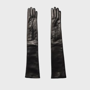 Könnte beinhalten: Ein Paar lange, schwarze Lederhandschuhe. Ein Handschuh hat eine dekorative Klappe mit drei kleinen Knöpfen. Die Handschuhe sind so konzipiert, dass sie weit über das Handgelenk hinausreichen und einen eleganten Look bieten. Die Handschuhe werden vor einem schlichten Hintergrund präsentiert.