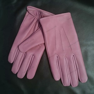 Puede incluir: Un par de guantes de cuero rosa. Los guantes tienen una superficie lisa y texturizada y están hechos de cuero de alta calidad.
