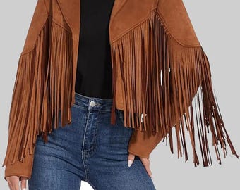May include: Brown suede jacket with long fringe detailing on the sleeves and back. The jacket has a classic collar and a tailored fit. The model is wearing blue jeans and a black top. The jacket is a stylish outerwear piece.
