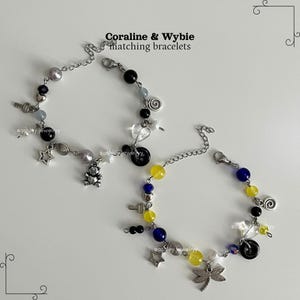 May include: Two matching bracelets with silver chains, featuring beads in black, yellow, blue, and grey. Charms include stars, keys, a teddy bear, and a dragonfly. The text "Coraline & Wybie matching bracelets" is visible.