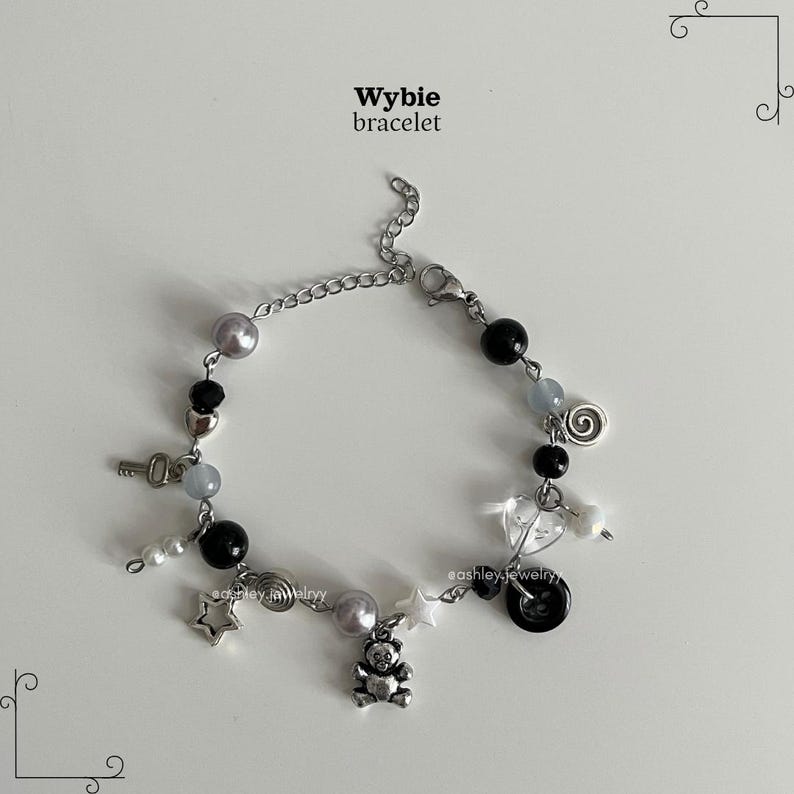 May include: A Wybie bracelet with a silver chain, adorned with charms like a key, stars, a teddy bear, and beads in black, grey, and pearl. It fastens with a lobster clasp.