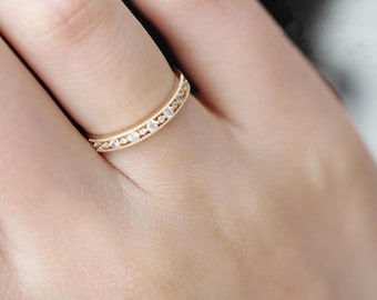 May include: A delicate gold band ring with a row of small, clear gemstones.