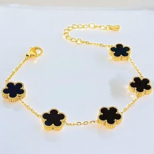 May include: A gold chain bracelet with five black clover charms. The charms are set in gold and have a detailed design.
