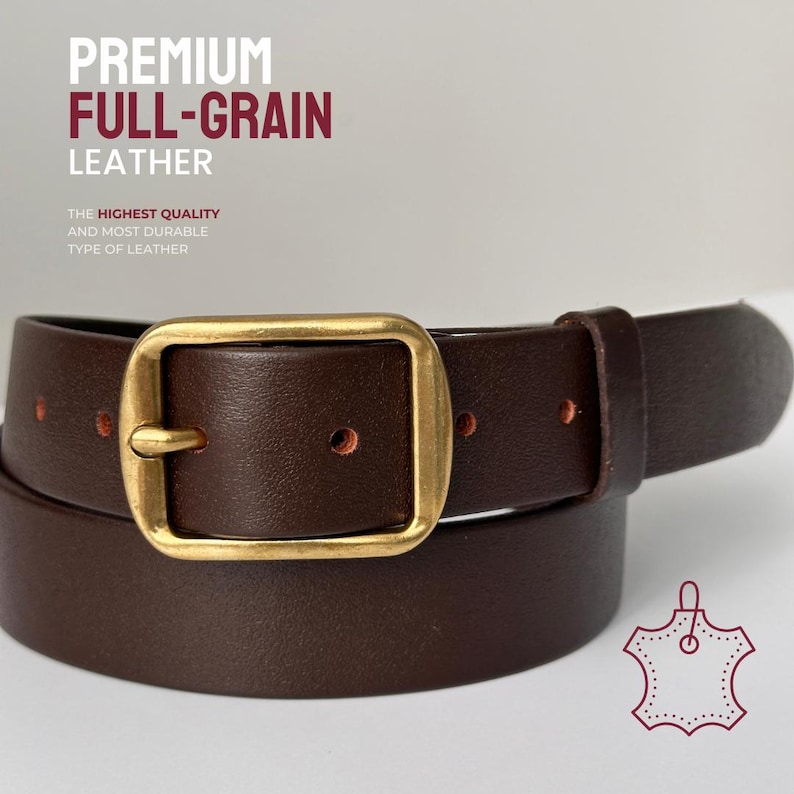 May include: A dark brown leather belt featuring a rectangular brass-toned buckle and a single leather keeper. The text PREMIUM FULL-GRAIN LEATHER and THE HIGHEST QUALITY AND MOST DURABLE TYPE OF LEATHER are visible above the belt.