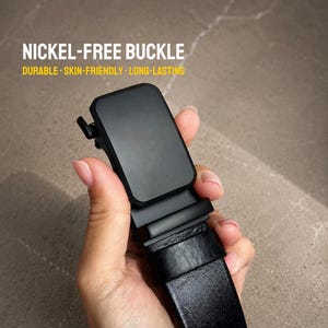 May include: A black belt with a rectangular matte black buckle. The text NICKEL-FREE BUCKLE DURABLE SKIN-FRIENDLY LONG-LASTING is printed in white and yellow above the buckle. The belt strap features a textured black leather-like finish.