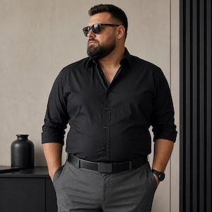 Könnte beinhalten: Ein schwarzes langärmeliges Hemd mit klassischem Kragen, kombiniert mit einer grauen Hose und einem schwarzen Gürtel. Das Hemd hat eine Knopfleiste auf der Vorderseite und lange Ärmel. Das Outfit wird durch eine dunkle Sonnenbrille ergänzt.