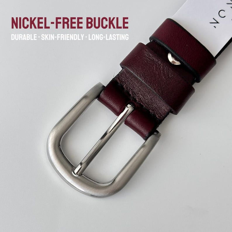 May include: A deep burgundy leather belt featuring a brushed silver-tone nickel-free buckle. The text NICKEL-FREE BUCKLE, DURABLE, SKIN-FRIENDLY, LONG-LASTING is printed in the upper left corner of the image, with a white tag visible.
