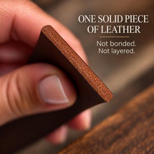 May include: A thick, brown leather strip with a visible cross-section showing a solid, non-layered texture. The text on the image reads: ONE SOLID PIECE OF LEATHER. Not bonded. Not layered.