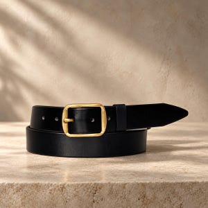 May include: A black leather belt featuring a rectangular brass-toned metal buckle. The belt strap is smooth and includes a matching black leather keeper loop near the buckle, with visible adjustment holes along the length of the strap.