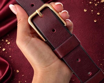 Cinturón de piel burdeos: hebilla dorada texturizada, elegante accesorio de piel color rojo vino para mujer.