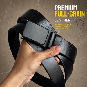 May include: A black full-grain leather belt with a solid black rectangular buckle. The text on the image reads: PREMIUM FULL-GRAIN LEATHER. THE HIGHEST QUALITY AND MOST DURABLE TYPE OF LEATHER. A leather hide icon is also visible on the right side.