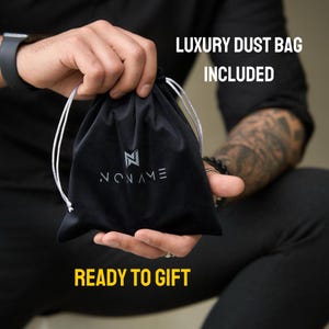 May include: A black drawstring dust bag featuring a white logo and the text NONAME printed on the front. The bag includes white drawstrings and is accompanied by the text LUXURY DUST BAG INCLUDED and READY TO GIFT displayed in the image.