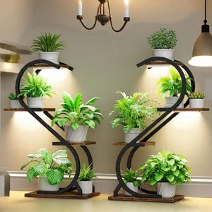 May include: Two black metal plant stands with multiple shelves, each holding various potted green plants. The stands have a curved design and built-in lights. The plants are in white pots, creating a contrast with the dark metal.