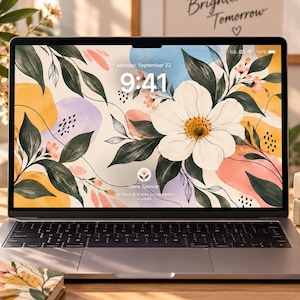 Può includere: Un computer portatile che mostra uno sfondo floreale con un fiore bianco, foglie verdi e forme astratte. Lo schermo indica l'ora 9:41 e la data lunedì 22 settembre. Il portatile è dotato di una tastiera grigio scuro e un telaio metallico.