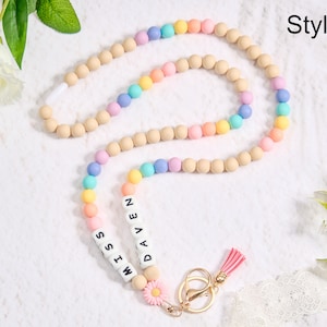 Puede incluir: Un cordón de cuentas de arcoíris pastel con el texto "MISS DAVEN" en cuentas de letras blancas. El cordón presenta un cierre dorado, una borla rosa y un pequeño dije de margarita. Las cuentas son en tonos de rosa, amarillo, azul y verde.