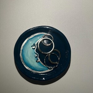 May include: A blue and white ceramic ring dish with a crescent moon design. The dish is decorated with silver paint and has a glossy finish.