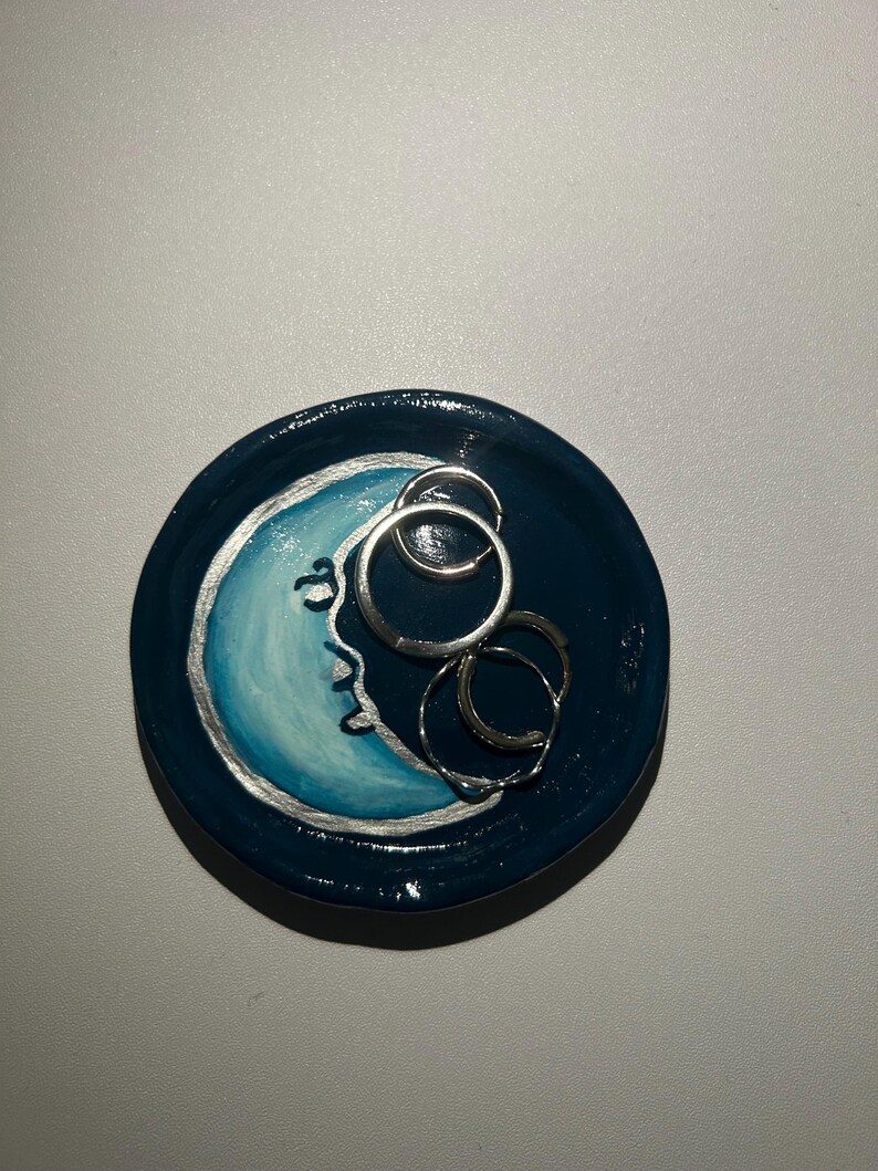 May include: A blue and white ceramic ring dish with a crescent moon design. The dish is decorated with silver paint and has a glossy finish.