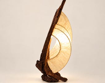 May include: A table lamp featuring a curved, textured piece of dark brown driftwood as a base and vertical support, paired with a translucent, off-white, semi-circular shade that emits a warm, soft glow from within its curved structure.