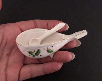 May include: A white ceramic salt cellar shaped like a bird with a small spoon. The cellar is decorated with green holly leaves and red berries.