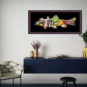 May include: A colorful, framed artwork of a fish, featuring a black background. The fish is composed of various shapes and colors, including red, yellow, blue, and green. The artwork is displayed on a white brick wall, above a dark blue cabinet.