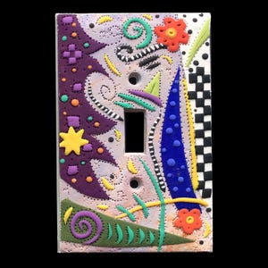 May include: A light switch cover with a colorful abstract design. The design features purple, blue, yellow, green, orange, black, and white colors. The switch cover is made of ceramic and has a textured surface.