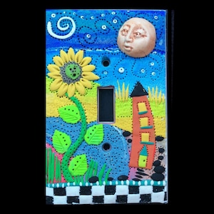 May include: A light switch cover with a whimsical design featuring a sunflower, a house, a moon with a face, and a checkered pattern.