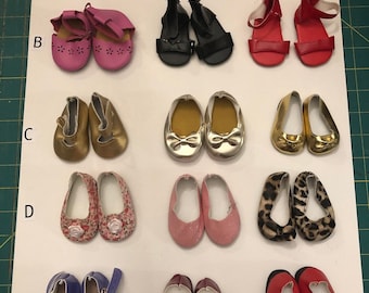 May include: A collection of 15 pairs of doll shoes in various colors and styles, including white, pink, black, gold, red, purple, and brown. The shoes are arranged in five rows of three pairs each, labeled A through E.