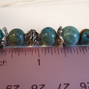 May include: A close-up of a turquoise and brown beaded necklace with silver accents. The beads are lined up on a ruler, showing that they are approximately 1 inch in diameter.
