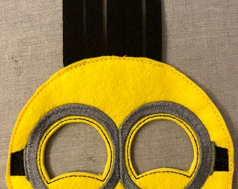 May include: Yellow felt eye mask with black felt hair and gray felt goggles. The mask is designed to look like a Minion from the Despicable Me movies.