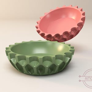 Puede incluir: Dos cuencos decorativos, uno verde y otro rosa, con un diseño geométrico texturizado. Los cuencos están hechos de un material liso y brillante y tienen una forma redondeada.