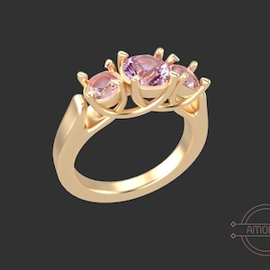May include: A gold ring featuring three pink gemstones set in a delicate, interwoven design.