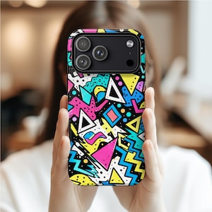 Könnte beinhalten: Eine schwarze Smartphone-Hülle mit einem lebendigen geometrischen Design im 80er-Jahre-Stil. Die Hülle zeigt ein sich wiederholendes Muster aus Dreiecken, Zickzacklinien und anderen Formen in leuchtenden Farben wie Pink, Gelb, Blau und Weiß. Die Hülle hat ein glänzendes Finish.