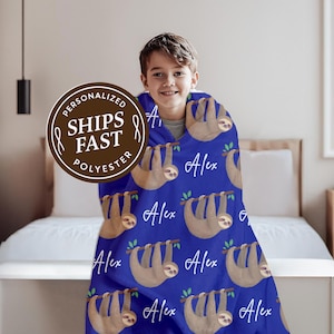 May include: A blue polyester blanket featuring a pattern of brown sloths hanging from green branches. The blanket has the name "Alex" in white script. A brown circular logo with the text "Personalized Ships Fast Polyester" is visible.