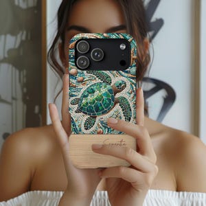 May include: A phone case featuring a mosaic-style sea turtle design in shades of green, blue, and brown. The top portion of the case has a detailed pattern with seashells and waves. The bottom is a light wood grain with the name "Samantha" engraved.