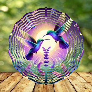 Pode incluir: Um moinho de vento de metal com um design circular que apresenta dois beija-flores em voo sobre um fundo roxo e dourado com flores de lavanda. Os beija-flores são azuis, verdes e roxos.