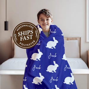 May include: A blue polyester blanket featuring white rabbit silhouettes and the name "Jack" in a script font. The blanket is wrapped around a person. The image also includes a brown circular sticker with the text "Ships Fast".