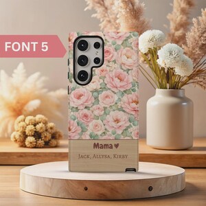 Pode incluir: Capa de telefone com um padr&atilde;o floral de rosas cor-de-rosa e folhas verdes. A parte inferior tem um acabamento com efeito de madeira, com a palavra "Mama" e os nomes "Jack, Allysa, Kirby". O texto "FONT 5" est&aacute; no canto superior esquerdo.