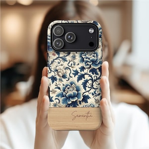 Pode incluir: Uma capa de telefone com um design floral em tons de azul e creme. A parte superior apresenta um conjunto de c&acirc;meras. A se&ccedil;&atilde;o inferior tem uma apar&ecirc;ncia de gr&atilde;o de madeira com o nome "Samantha" em it&aacute;lico.