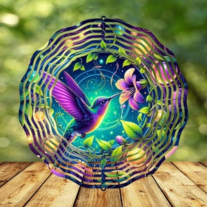 Puede incluir: Un molinillo de viento de metal con un diseño de colibrí colorido. El colibrí está representado con plumas moradas, azules y verdes, y está bebiendo néctar de una flor rosa. El fondo es un patrón de remolino de azul, verde y dorado.