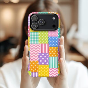 May include: A vibrant patchwork phone case with a mix of patterns such as polka dots, stripes, and zigzags. The case showcases a range of bright colours, including pink, yellow, green, and purple. The phone case has a camera module with three lenses.