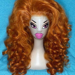 Może przedstawiać: Żywa pomarańczowa peruka z bujnymi, kręconymi włosami ułożonymi na głowie manekina. Głowa manekina ma pomalowaną twarz z dużymi oczami i różowymi ustami. Peruka jest ustawiona na niebieskim tle.