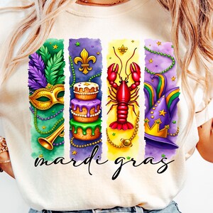 May include: A white t-shirt with a colorful design featuring a Mardi Gras mask, a cake, a crawfish, and a jester's hat. The text "Mardi Gras" is written below the design.