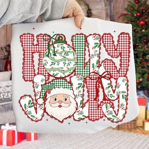 May include: A white Christmas-themed sweatshirt with the words "HOLY JOLLY" in a mix of red gingham, green gingham, and floral patterns. A Santa Claus face and a Christmas ornament are also featured.