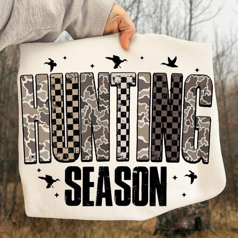 Puede incluir: Bolso tote color crema con las palabras "HUNTING SEASON" en un patr&oacute;n de camuflaje y cuadros. Siluetas de p&aacute;jaros y estrellas est&aacute;n dispersas alrededor del texto. El bolso es sostenido por una persona.