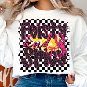 May include: White sweatshirt with a black and white checkered background. The text "Feisty and Spicy" is written in pink and black letters with a lemon and a pink crawfish graphic.