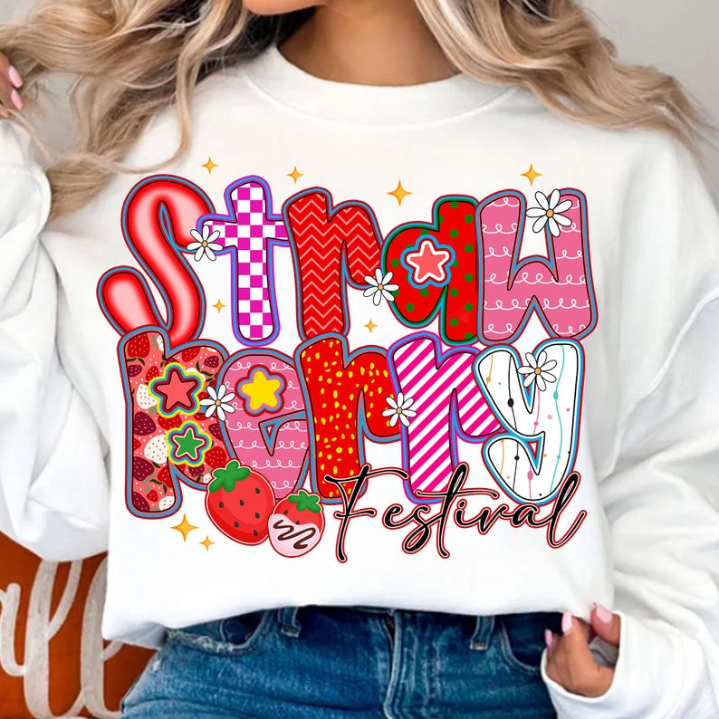 May include: White sweatshirt with a colourful "Strawberry Mommy Festival" graphic. The text features various patterns, including strawberries, gingham, and stripes, with floral accents and a strawberry illustration.