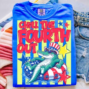 May include: Blue t-shirt with the text "Chill the Fourth Out" in red and yellow. The graphic features a cartoon alligator wearing sunglasses and an Uncle Sam hat, floating on a red, white, and blue inner tube. Stars and stripes complete the patriotic design.